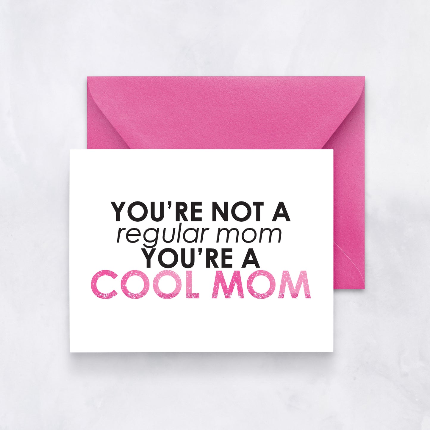 Greeting card with bold black and pink text reading “You’re not a regular mom, you’re a cool mom,” styled with a hot pink envelope.