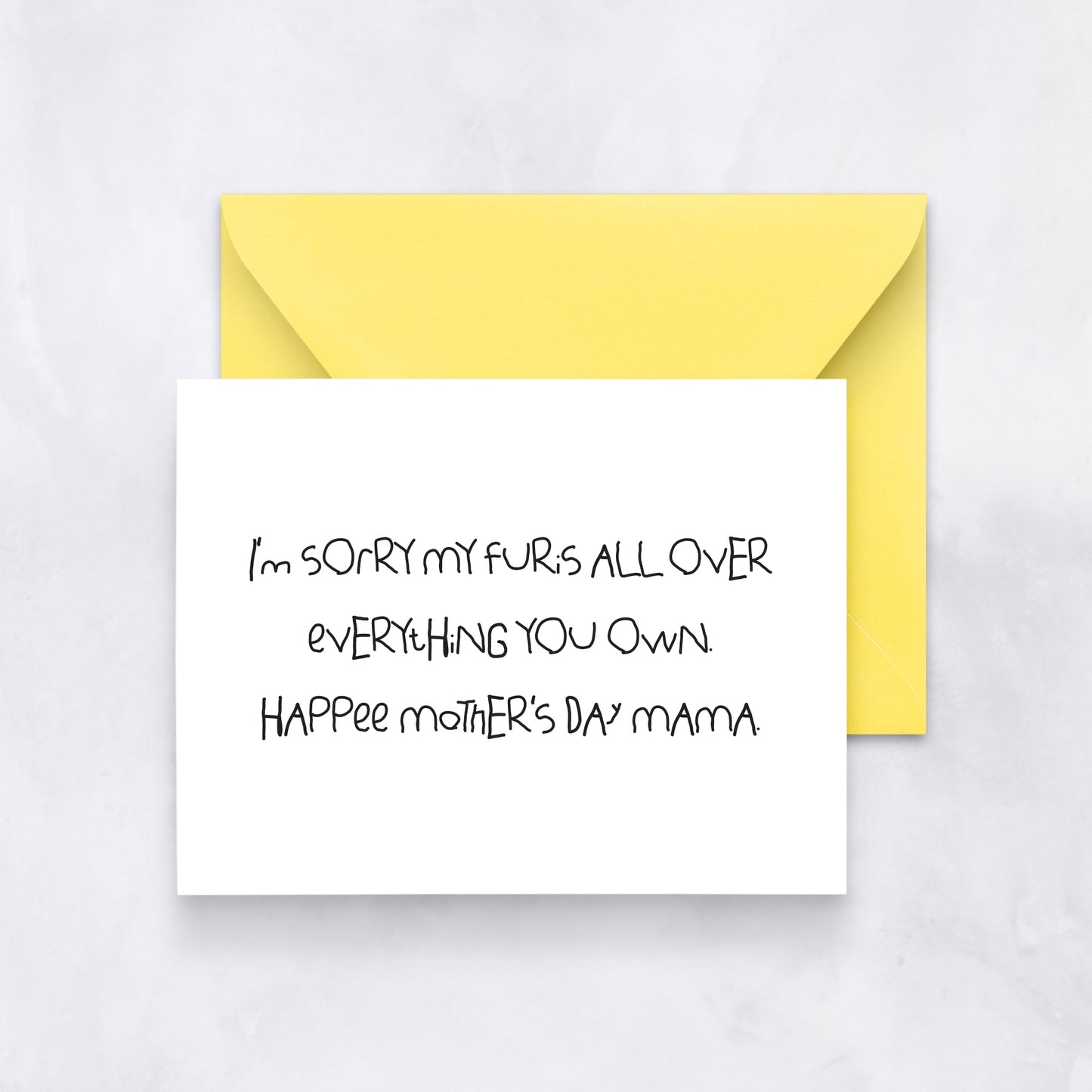White greeting card with handwritten text reading “I’m sorry my fur’s all over everything you own. Hap-Pee Mother’s Day Mama,” paired with a yellow envelope.