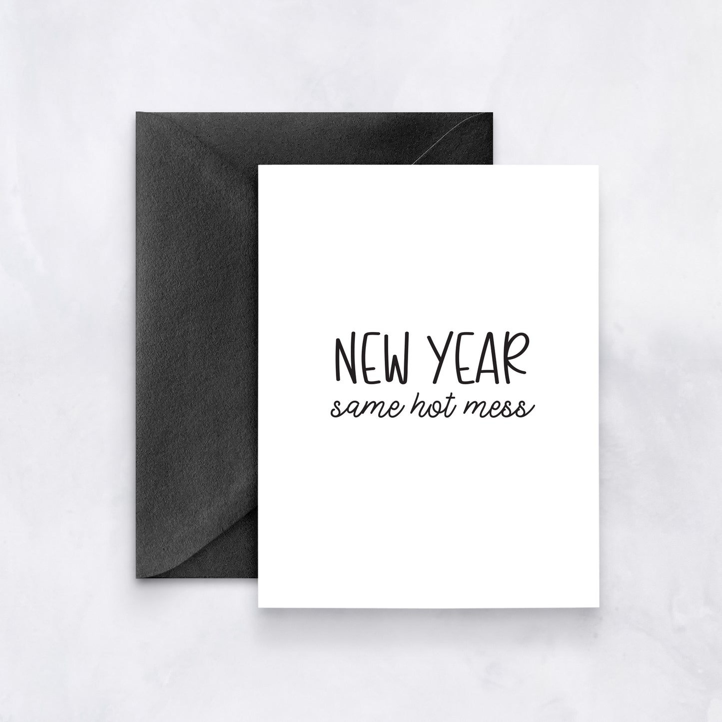 White greeting card with black text reading “New Year same hot mess,” paired with a black envelope.