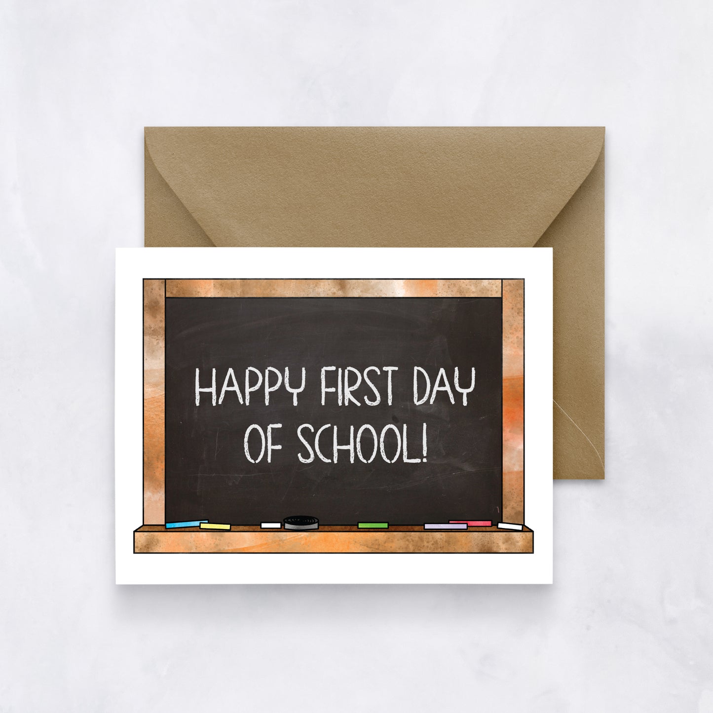 White card featuring a chalkboard illustration with “Happy first day of school!” text, paired with a brown envelope.