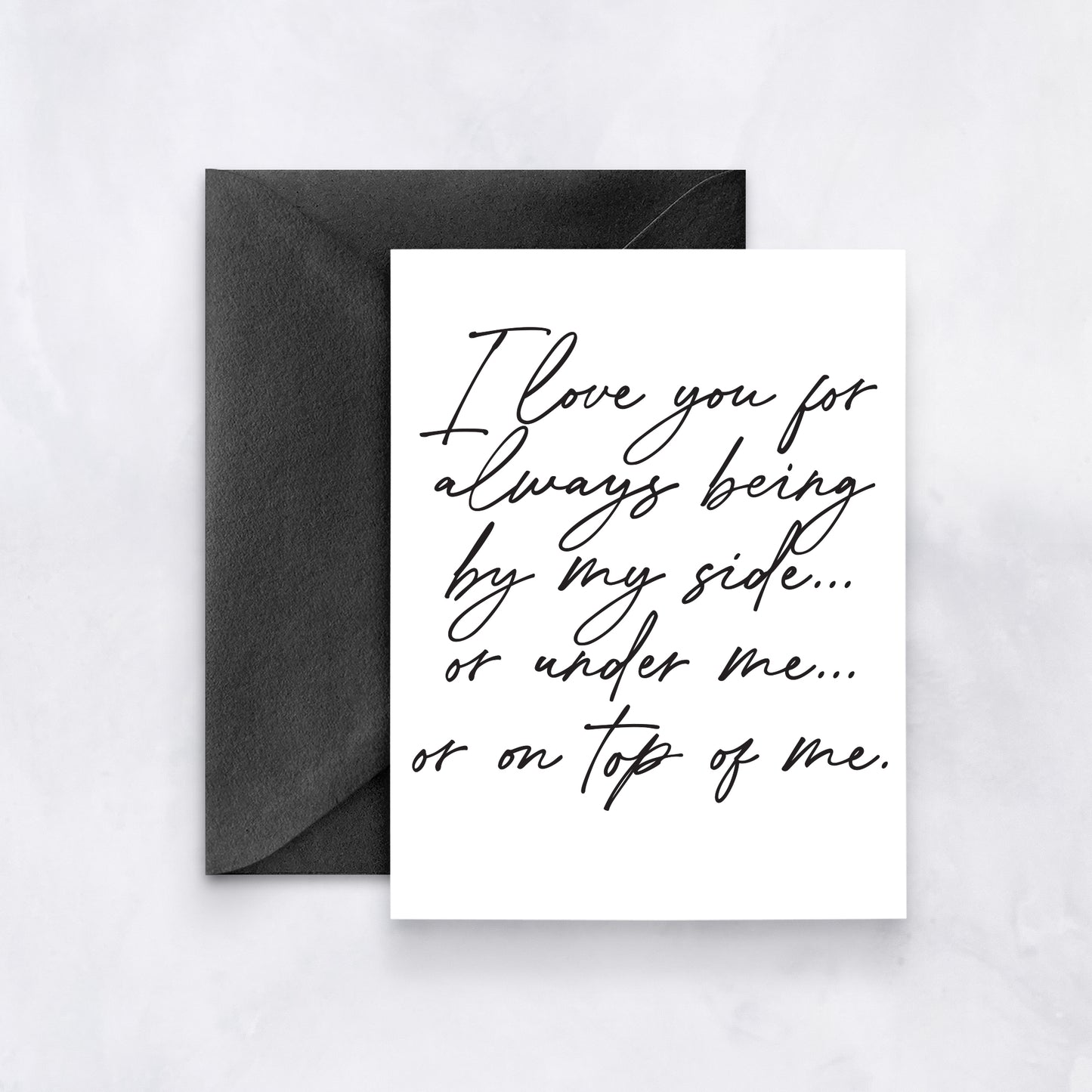 White card with black handwritten script reading “I love you for always being by my side… or under me… or on top of me,” styled with a black envelope.