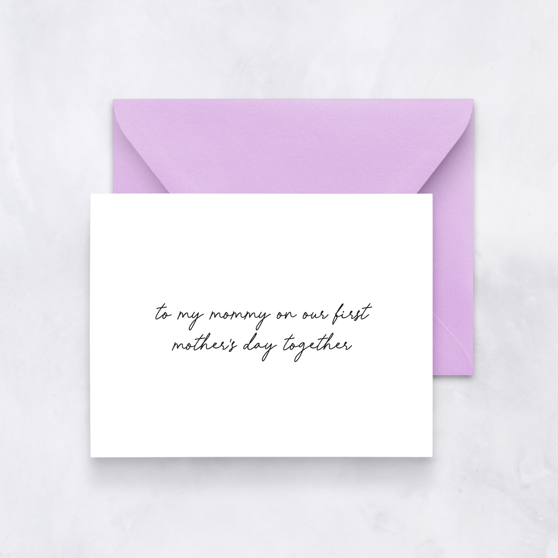 White greeting card with black handwritten text reading “to my mommy on our first Mother’s Day together,” styled with a lavender envelope.