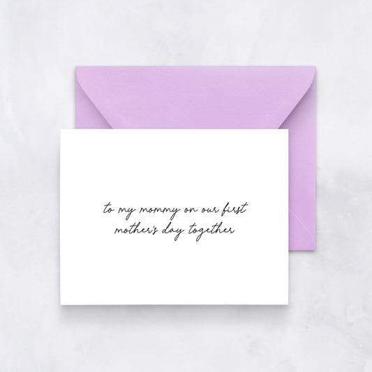 White greeting card with black handwritten text reading “to my mommy on our first Mother’s Day together,” styled with a lavender envelope.