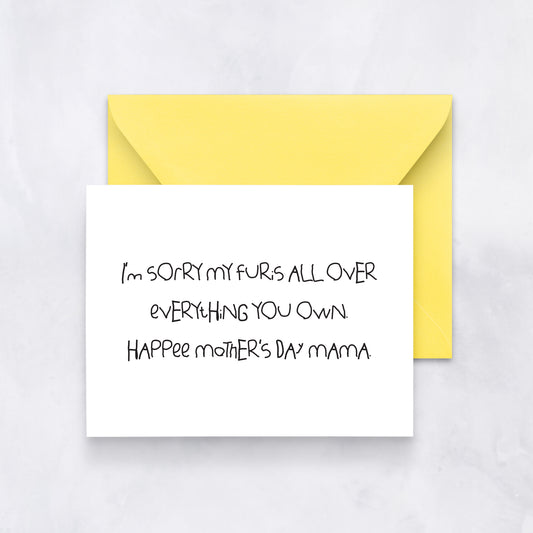 White greeting card with handwritten text reading “I’m sorry my fur’s all over everything you own. Hap-Pee Mother’s Day Mama,” paired with a yellow envelope.