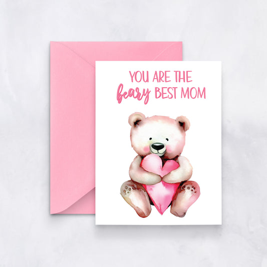 White greeting card with a watercolor teddy bear holding a pink heart and the message “You are the beary best mom,” styled with a pink envelope.