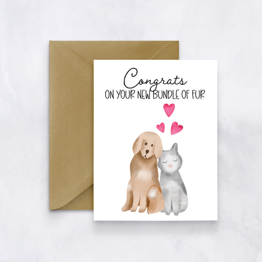 Greeting card featuring watercolor dog and cat illustration with pink hearts and the phrase “Congrats on your new bundle of fur,” paired with a brown envelope.