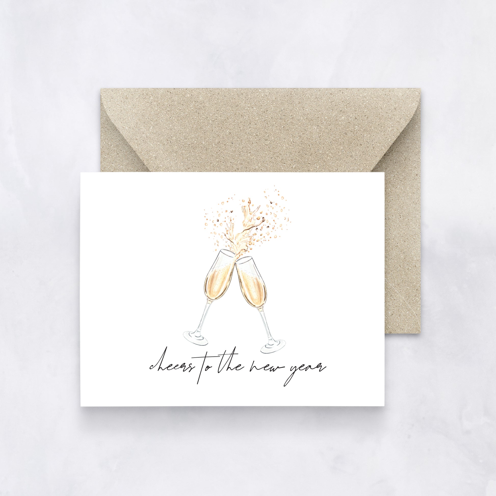 White greeting card with two watercolor champagne glasses clinking and text “cheers to the new year,” styled with a tan envelope.