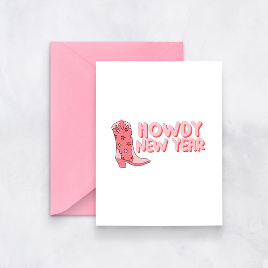 White greeting card with pink text reading “Howdy New Year” and a pink cowboy boot illustration, styled with a pink envelope.