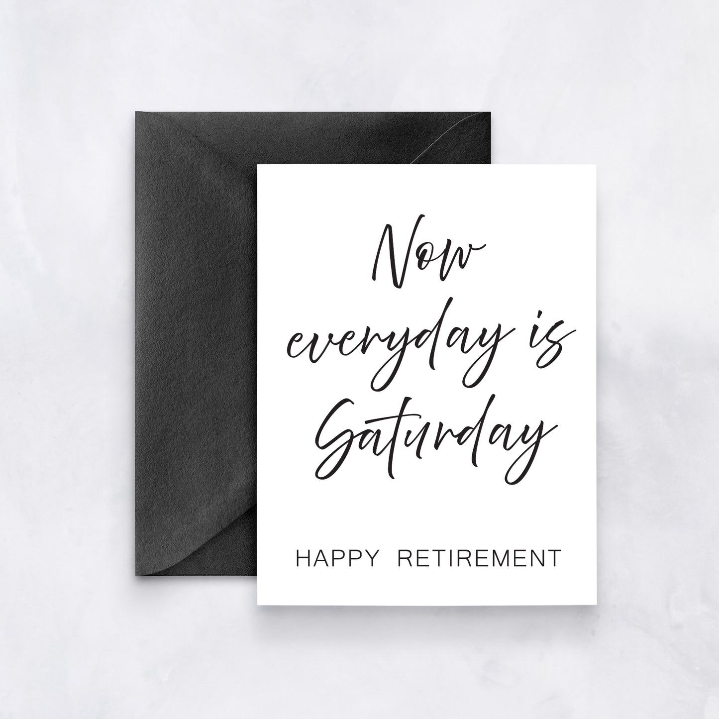White greeting card with black handwritten script reading “Now everyday is Saturday – Happy Retirement,” paired with a black envelope.