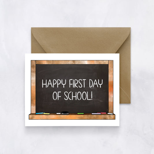 White card featuring a chalkboard illustration with “Happy first day of school!” text, paired with a brown envelope.