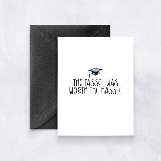 White card with graduation cap illustration and text “The tassel was worth the hassle,” paired with a black envelope.
