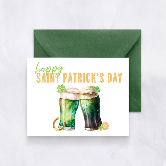White card with watercolor illustration of two green beers and text “Happy Saint Patrick’s Day” in green and gold, paired with a dark green envelope.