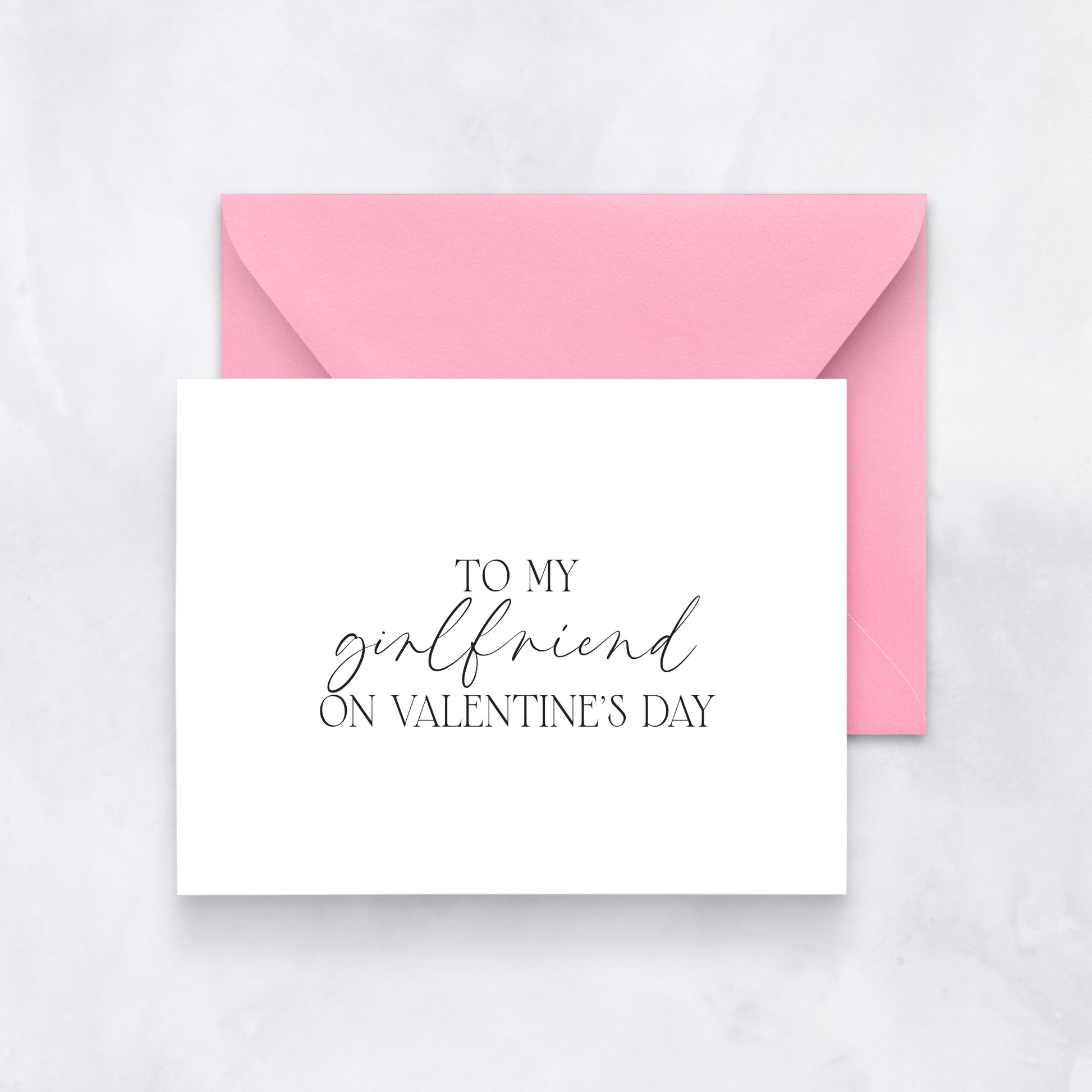 White card with elegant black script reading “To my girlfriend on Valentine’s Day,” paired with a pink envelope.