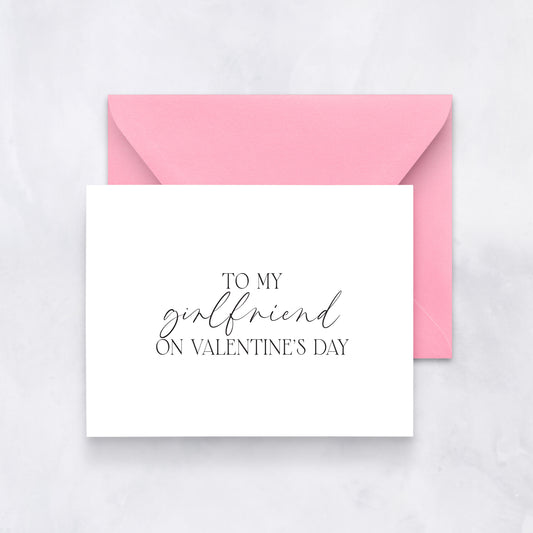 White card with elegant black script reading “To my girlfriend on Valentine’s Day,” paired with a pink envelope.