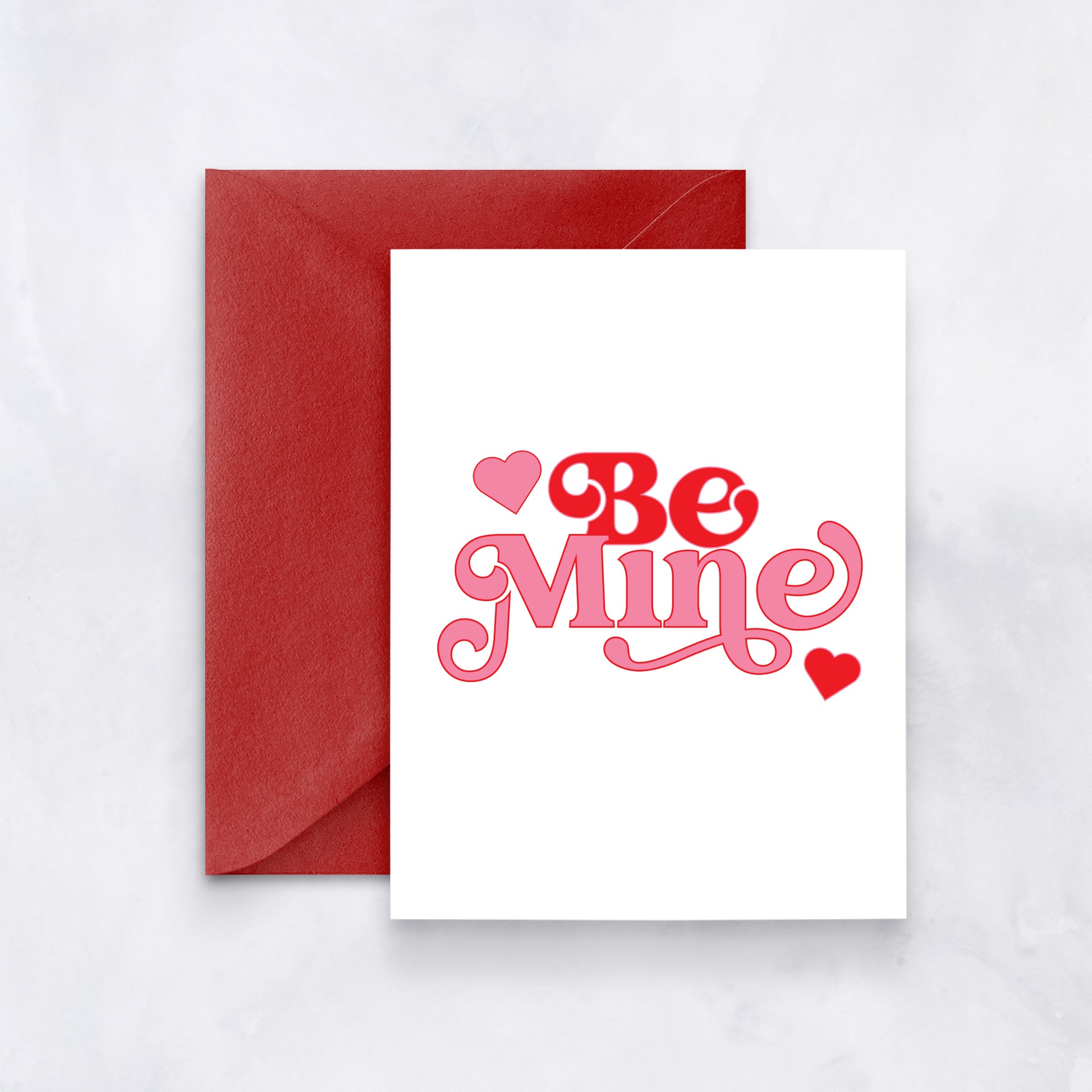 White card with red and pink retro-style text reading “Be Mine,” styled with a red envelope.