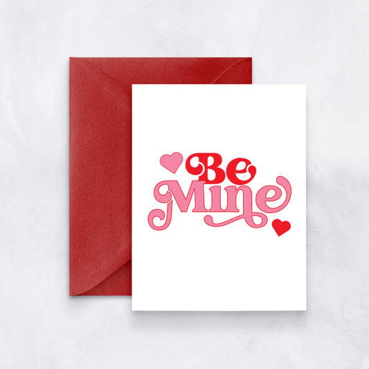 White card with red and pink retro-style text reading “Be Mine,” styled with a red envelope.