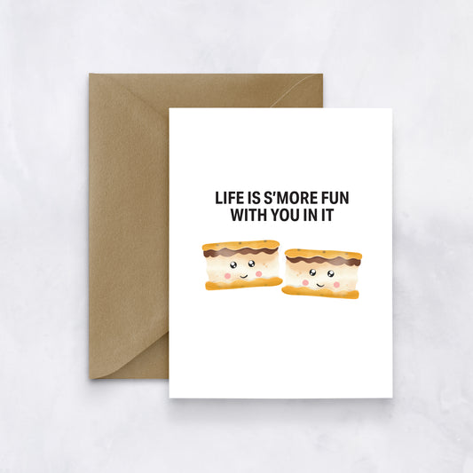White card with two smiling s’mores illustrations and black text reading “Life is s’more fun with you in it,” paired with a brown envelope.