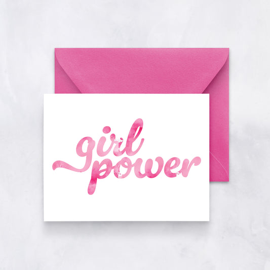 White card with pink watercolor script reading “girl power,” styled with a bright magenta envelope on a light marble backdrop.