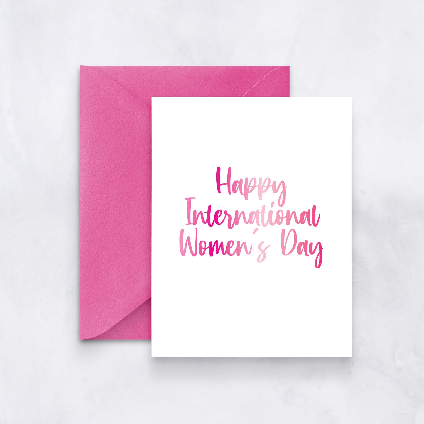 White card with pink gradient script reading “Happy International Women’s Day,” styled with a vibrant fuchsia envelope.