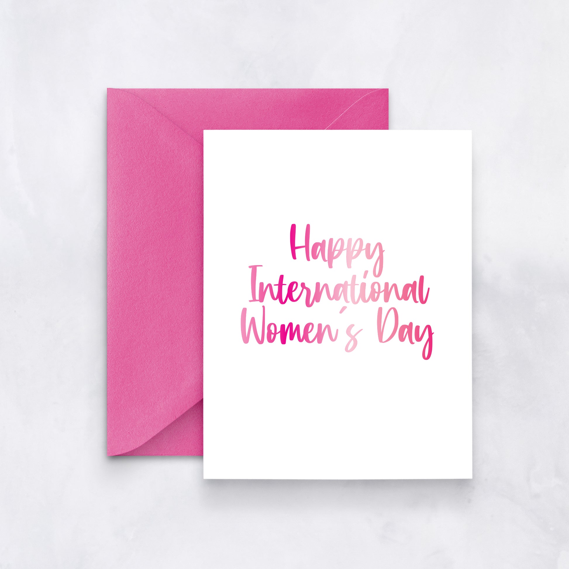 White card with pink gradient script reading “Happy International Women’s Day,” styled with a vibrant fuchsia envelope.