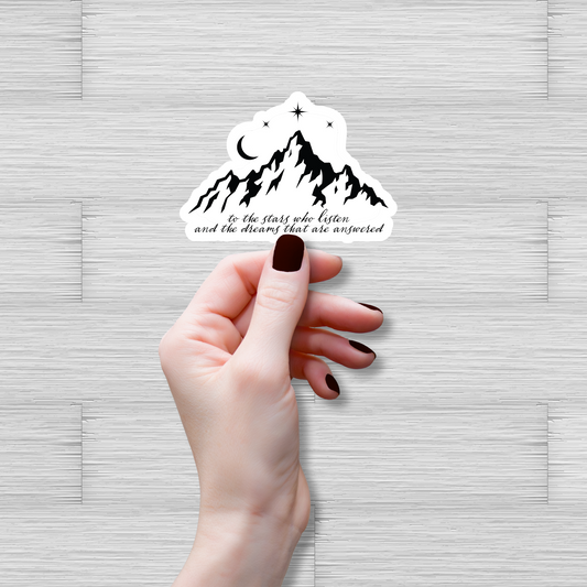 Hand holding a mountain-themed sticker with text on a light gray background
